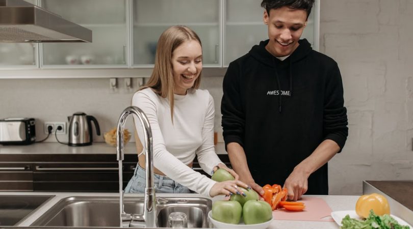 Smiling young couple cooking together in a modern kitchen, slicing fresh vegetables.