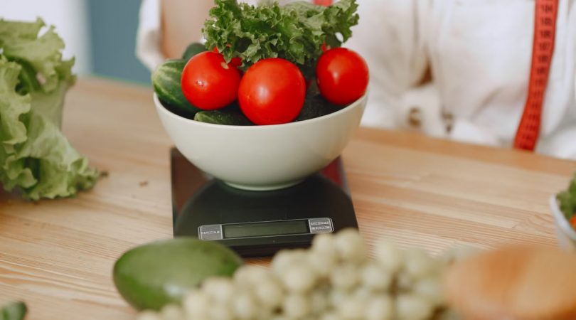 Colorful fresh vegetables including tomatoes and cucumbers on a kitchen scale for healthy eating.